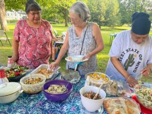 three women in the picnic line with food in front of them on a table 
