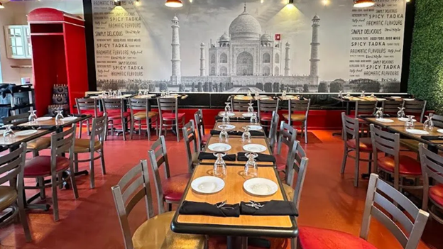 photo of Raj Saffron restaurant's interior with a Backdrop banner of the Taj Mahal and many empty tables throughout the room.